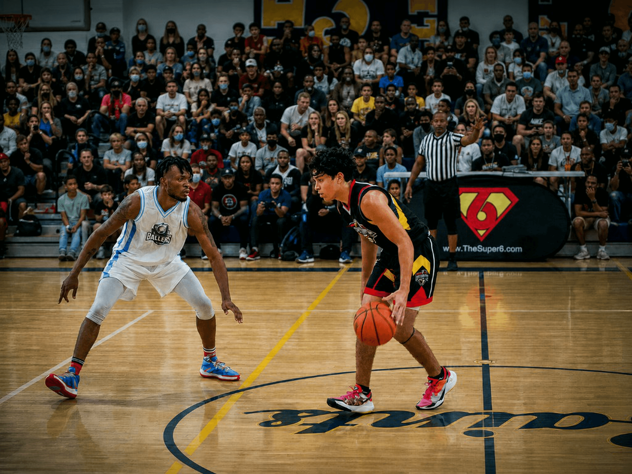 Two athletes face off one-on-one, Ballers defender vs opposing guard, Super6 crowd and banner behind them.