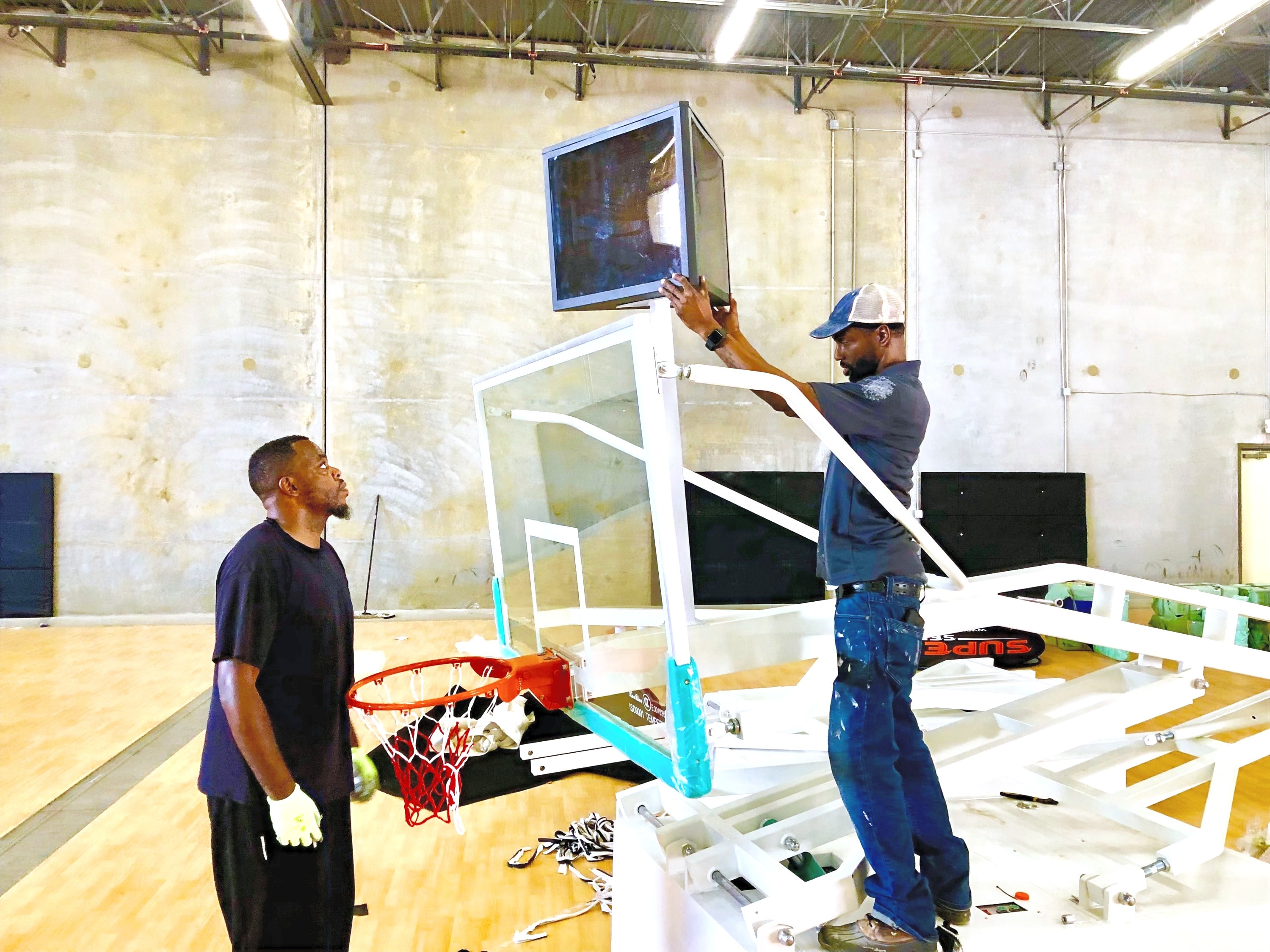 Two crew members assembling a basketball backboard in the venue